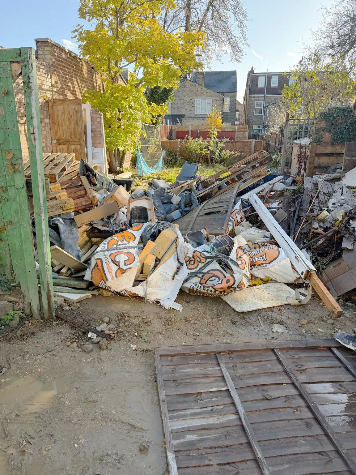 Before. A pile of timber, plasterboard and rubble bags stacked against the fence line.
