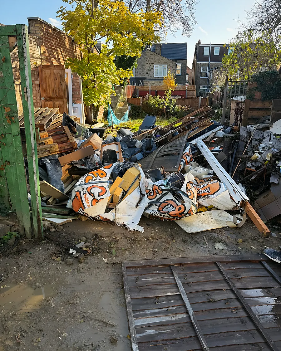 Timber, plasterboard and rubble bags piled against a garden fence
