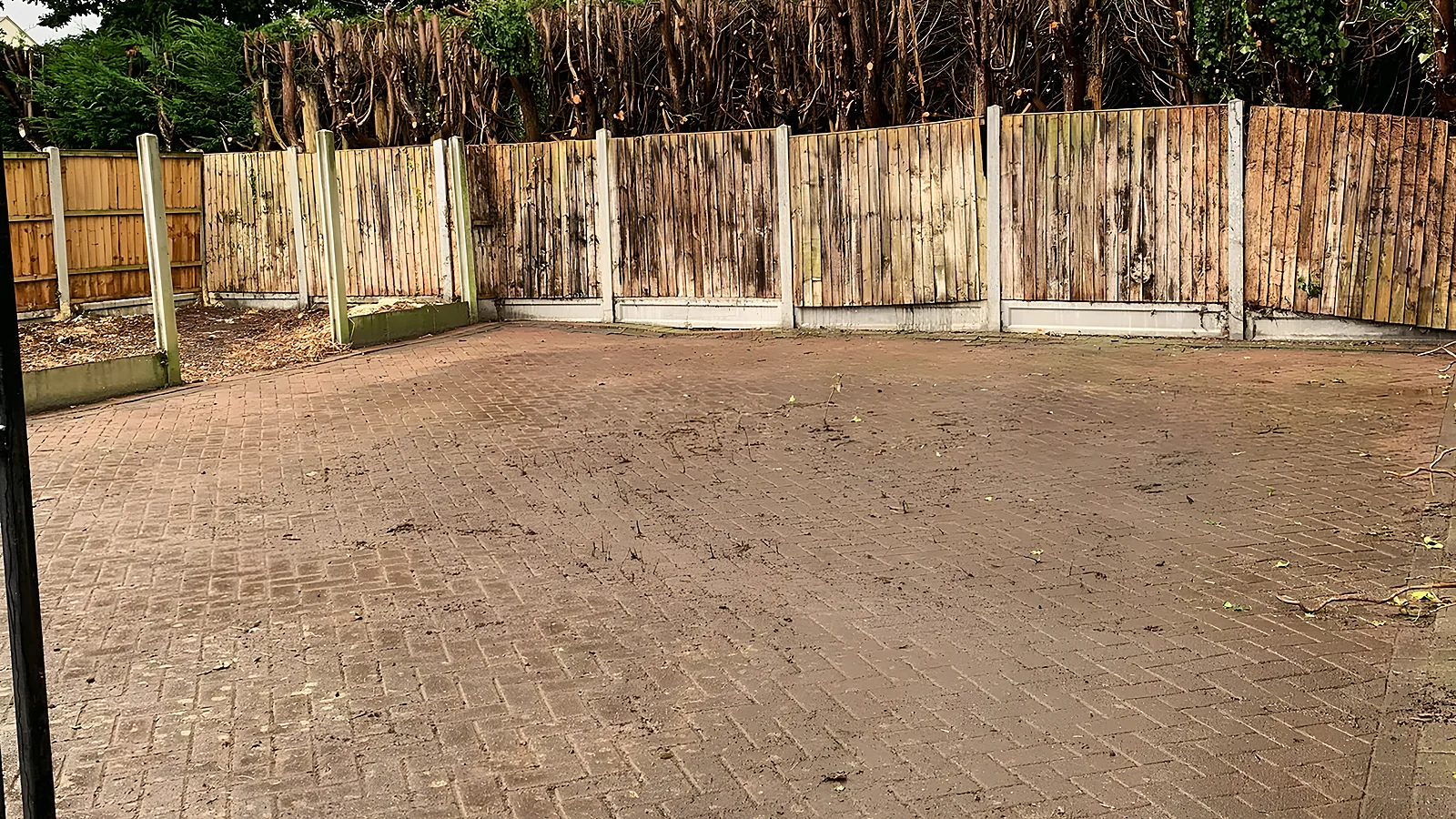 A block-paved yard swept clear, a new close-board fence and the hedge behind