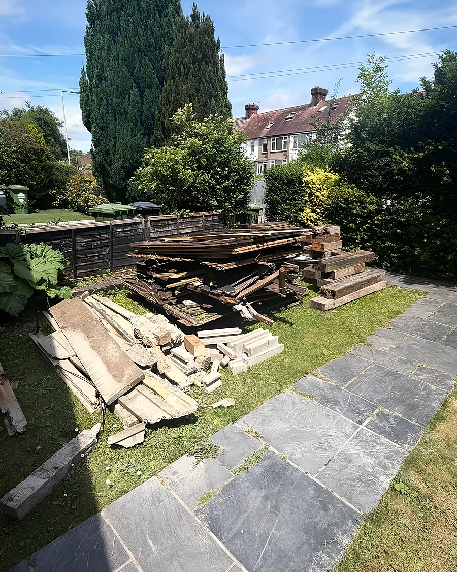A long pile of scrap timber across a lawn beside a slate path