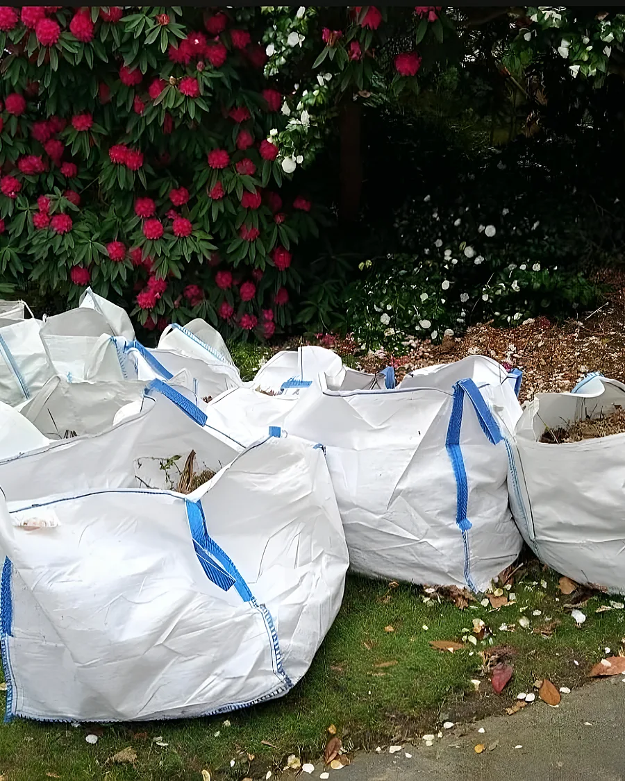 Six bulk bags of garden waste on a lawn under a flowering rhododendron