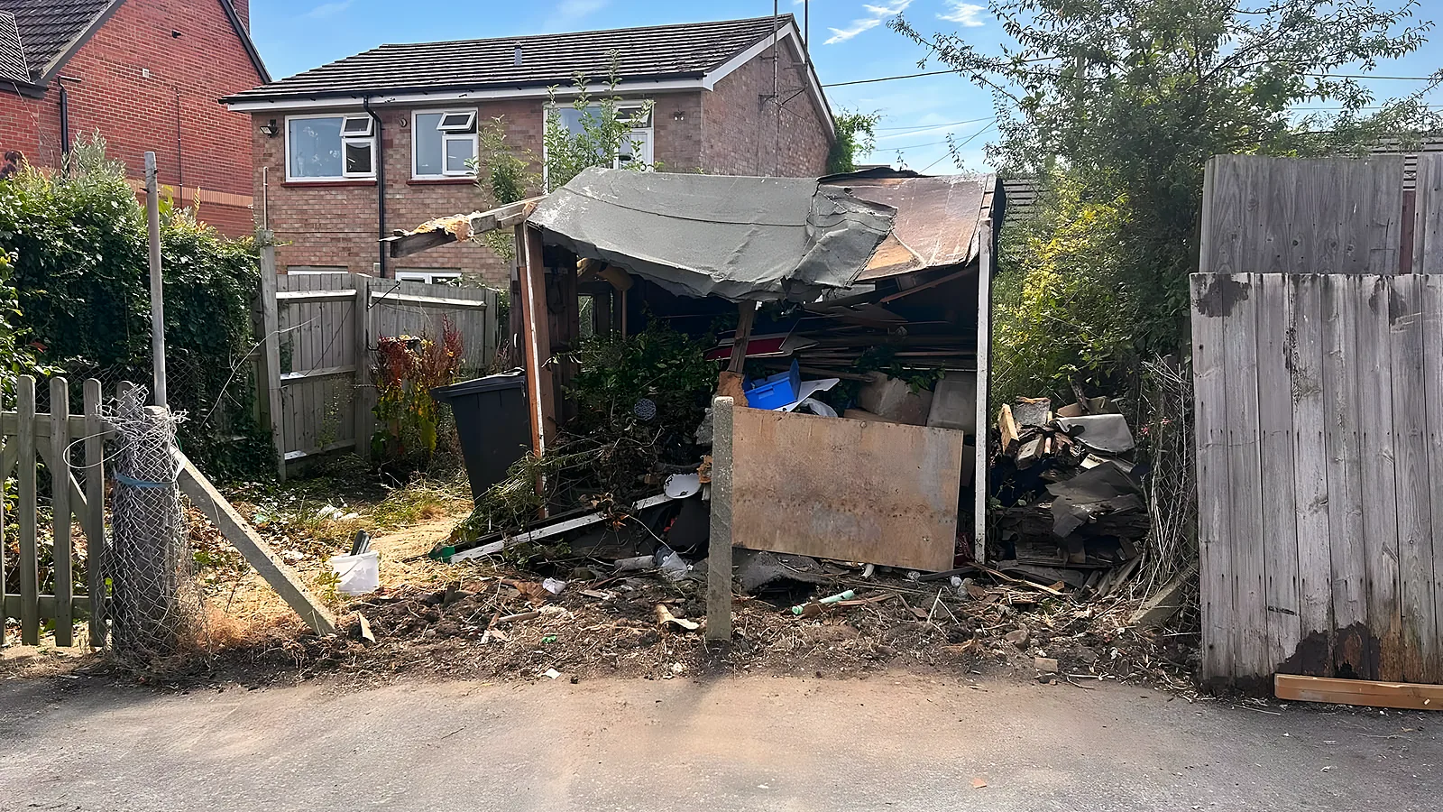 A collapsed outbuilding between two fences, its roof caved in