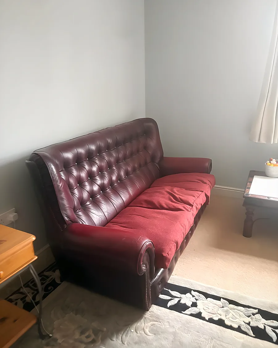 A living room with a red leather chesterfield sofa still in place