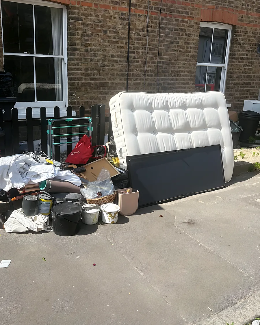 A house clearance load out on the pavement of a brick terrace: a mattress, a television and bags