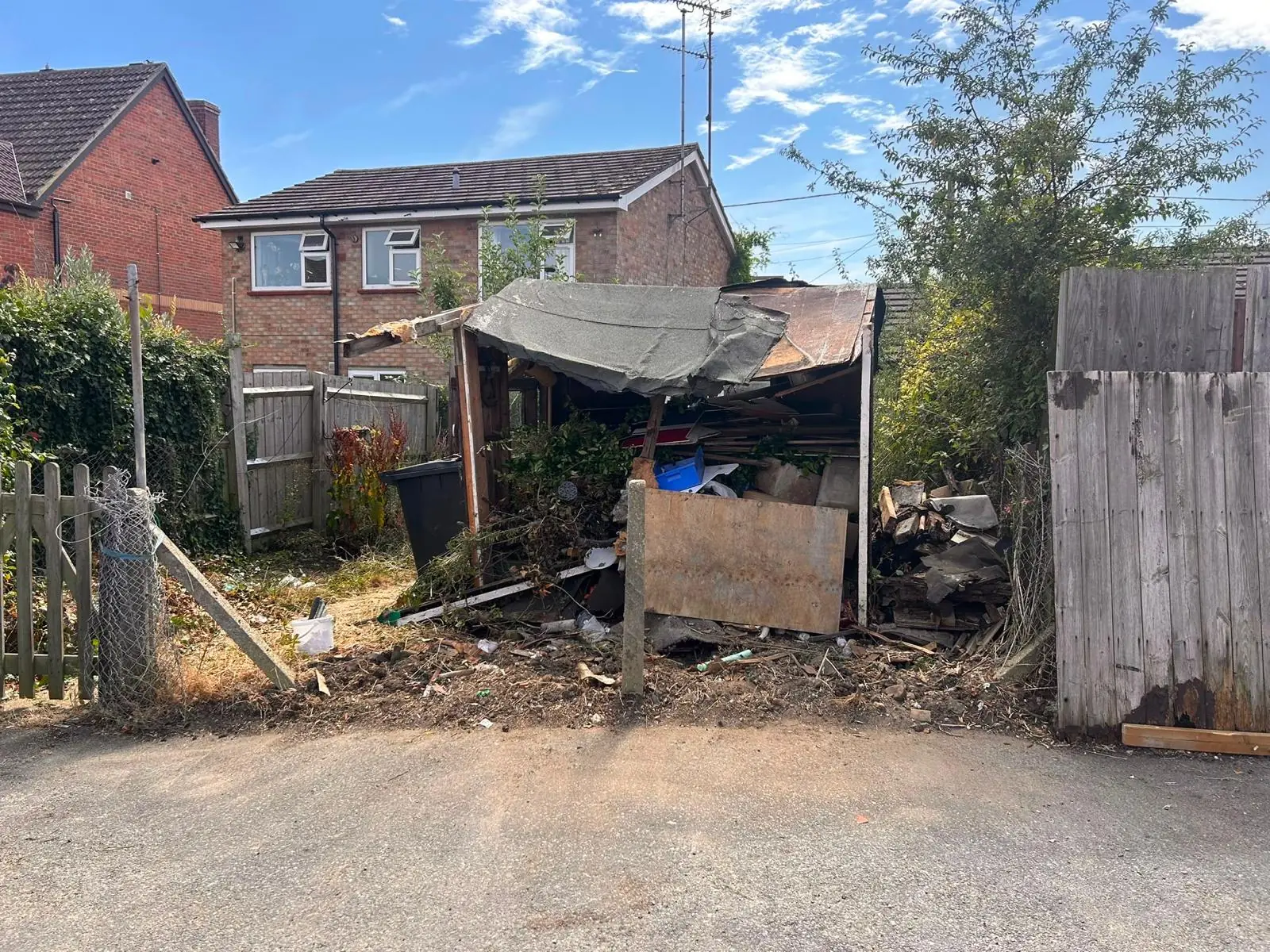 Before. A collapsed timber outbuilding at the end of a plot, behind a fence