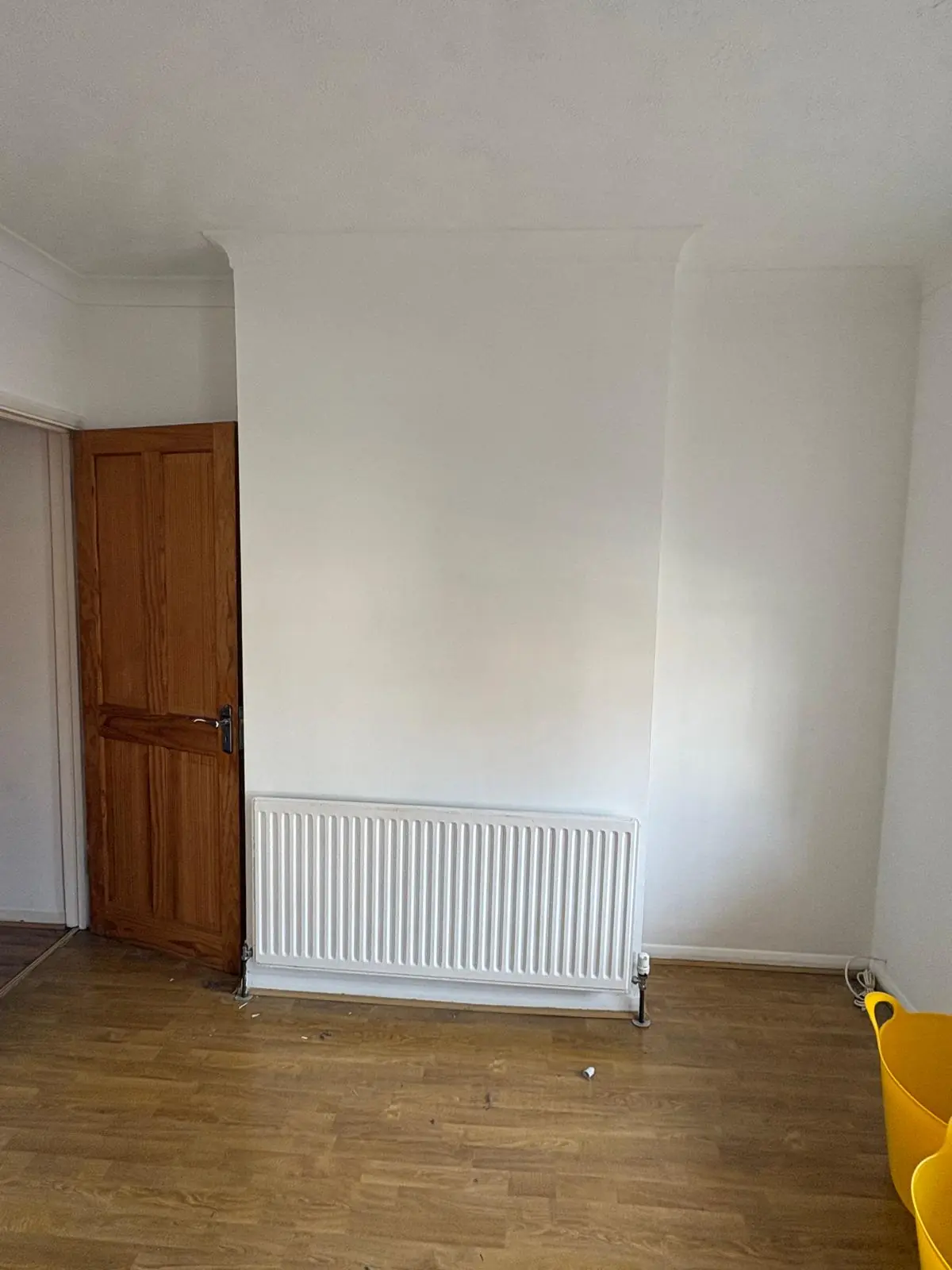 An empty room with a pine door, a radiator and a swept laminate floor